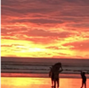 Student walking the beach at sunset with a surfboard
